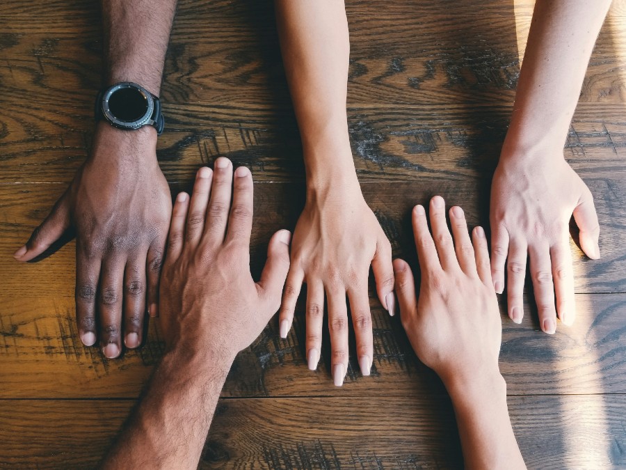 Cuatro manos encima de una mesa. Imagen de Unsplash por Clay Banks.